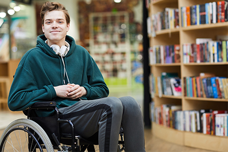 stock photo of teenager sitting in a wheelchair in a library.