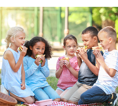 Children eating sandwiches on blanket enjoying a nice summer day.