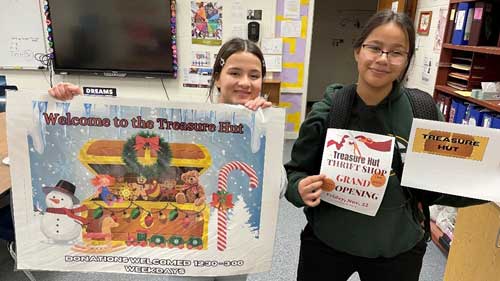 two smiling students hold up signage they created for their treasure hut store